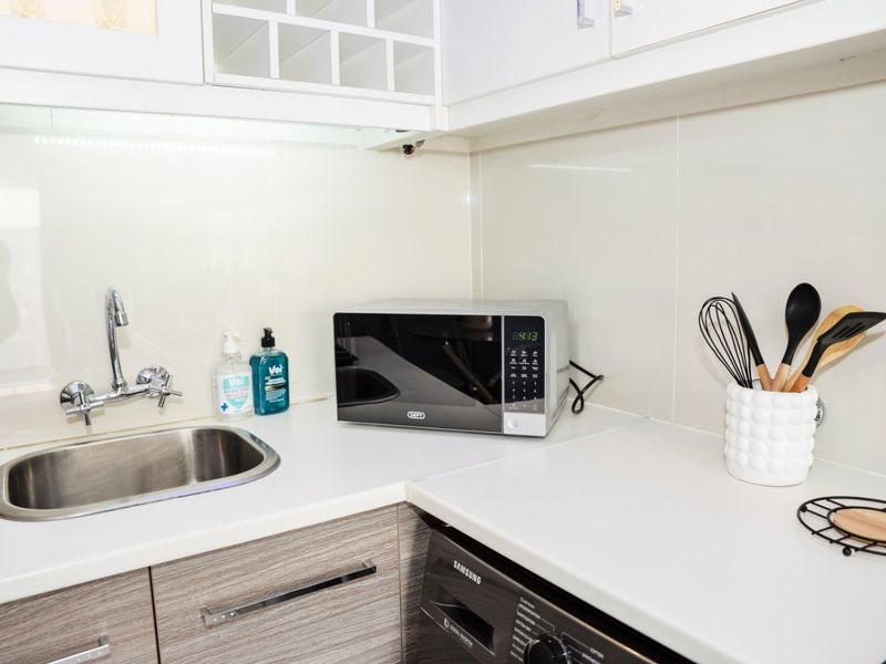 A clean and functional kitchen area featuring a stainless steel sink, modern chrome tapware, laminate countertops, and integrated cabinetry with a tiled splashback.