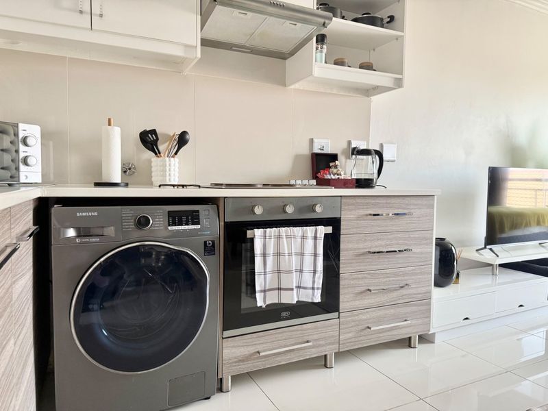 Modern kitchen featuring sleek laminated cabinetry, built-in oven, extractor fan, and integrated washing machine with clean tiled splashbacks and flooring.
