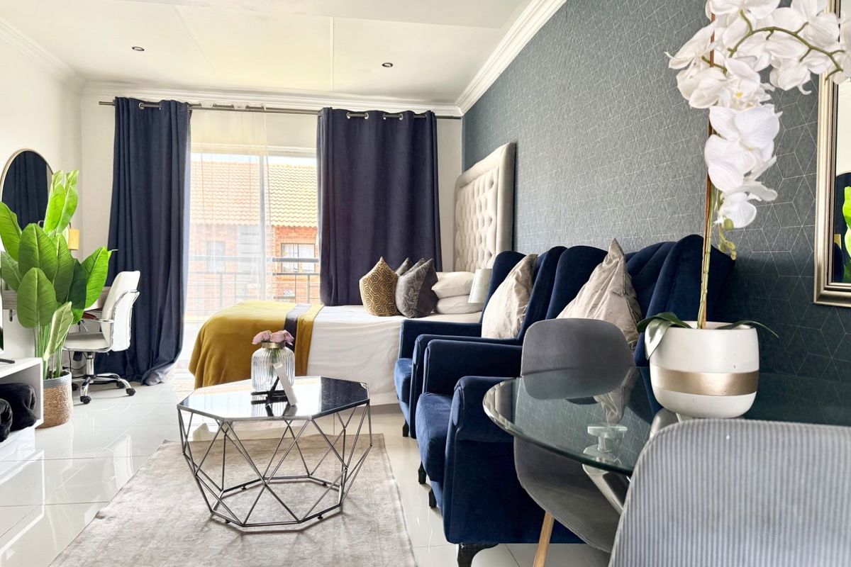 A well-maintained bedroom featuring tiled flooring, textured accent wallpaper, crown molding, and a sliding glass door providing natural light.