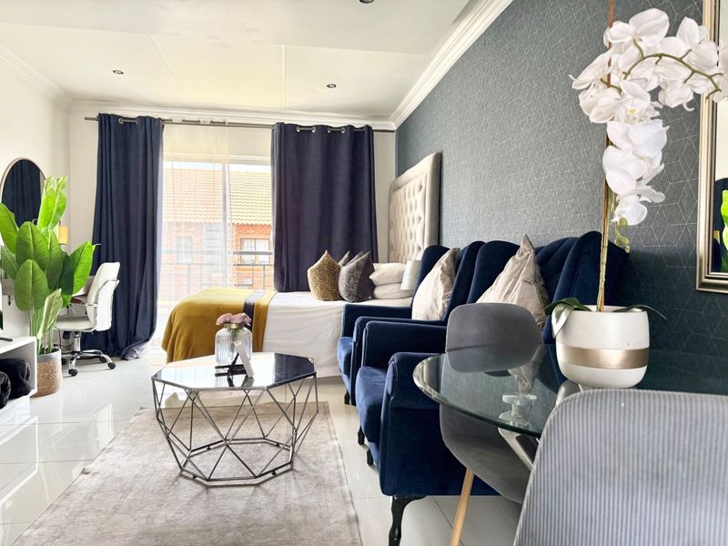 A well-maintained bedroom featuring tiled flooring, textured accent wallpaper, crown molding, and a sliding glass door providing natural light.