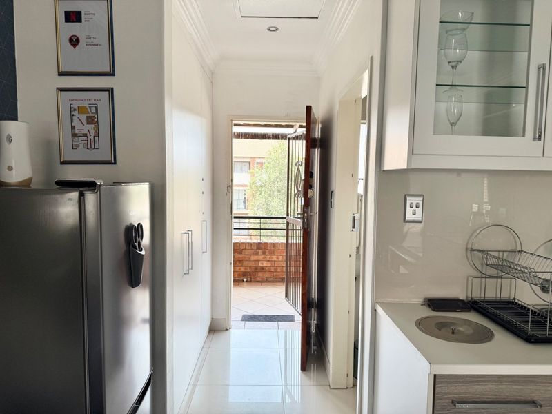 A bright kitchen area featuring white built-in cabinetry, tiled flooring, and direct access to an outdoor balcony through a security gate.