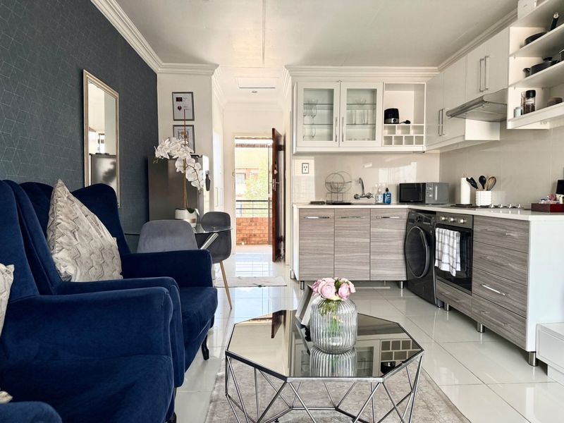 A modern open-plan living and kitchen area featuring sleek cabinetry, integrated appliances, tiled flooring, and elegant crown molding, leading to an exterior entrance.