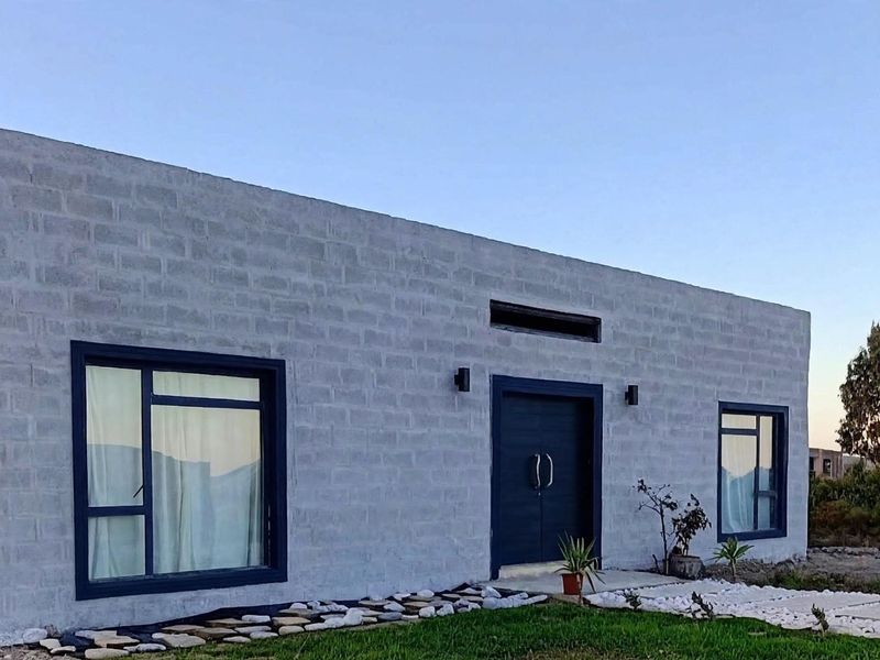 Modern single-story home featuring an exposed concrete block facade, dark window frames, and a prominent double-door entrance with minimalist exterior lighting.