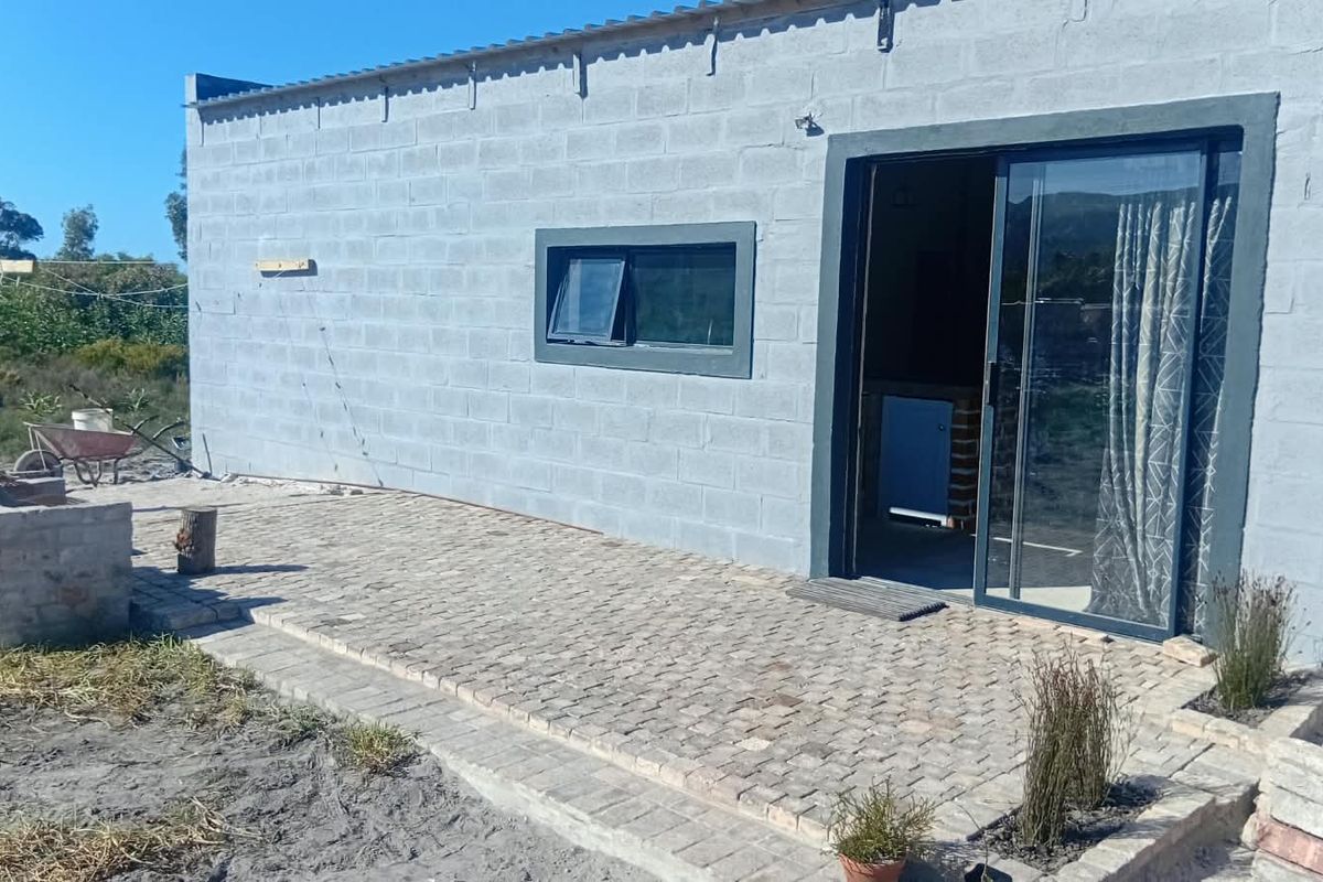 Rear exterior view featuring a paved patio area, built-in brick braai, and sliding glass door access to the main living space.