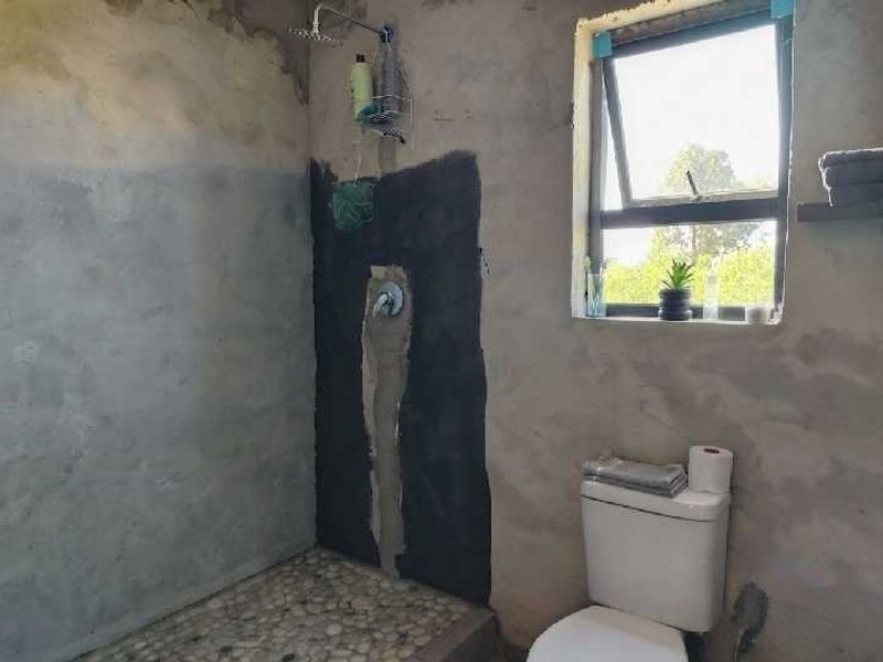 A bathroom in a state of renovation featuring a pebble-floored shower area, a toilet, and unfinished plaster walls requiring final finishes.