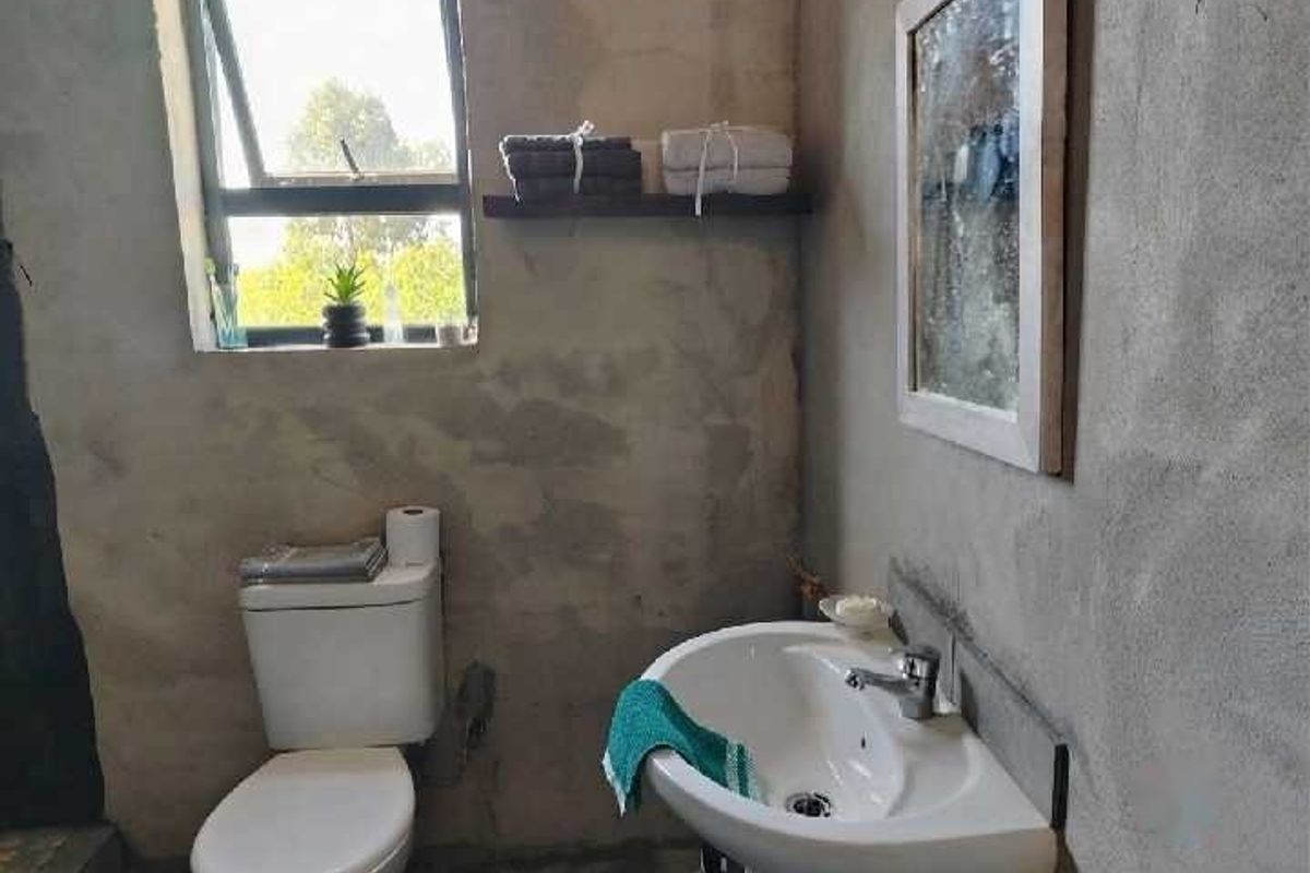A bathroom featuring a pedestal sink, toilet, and casement window, currently with unfinished raw concrete wall surfaces.
