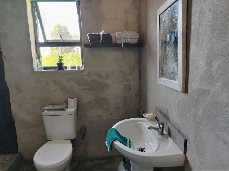 A bathroom featuring a pedestal sink, toilet, and casement window, currently with unfinished raw concrete wall surfaces.