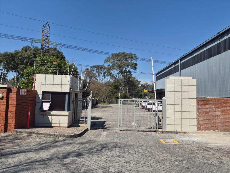 Industrial property entrance featuring a secure guard house, automated boom gate, perimeter brick walling, and electric fencing for enhanced site security.