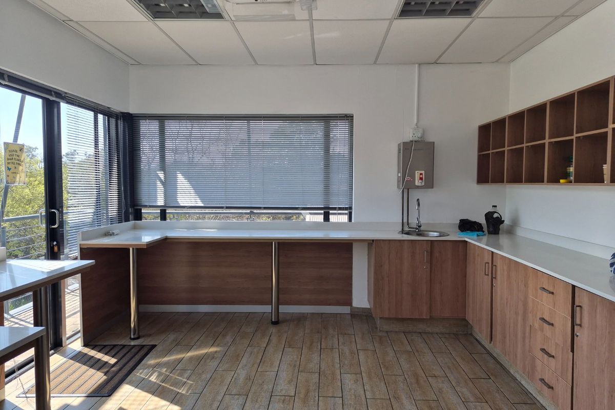 A clean, functional industrial kitchenette featuring wood-look cabinetry, laminate countertops, a stainless steel sink, and ample natural light from large sliding glass doors.