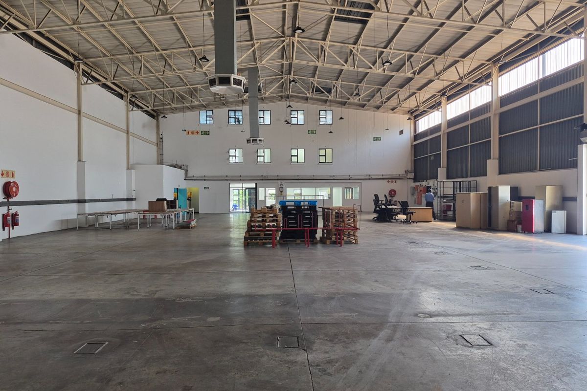 Spacious industrial warehouse featuring high ceilings with exposed steel trusses, concrete flooring, and ample natural light through high-level windows.