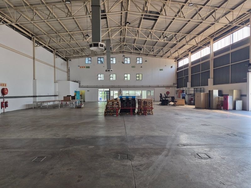 Spacious industrial warehouse featuring high ceilings with exposed steel trusses, concrete flooring, and ample natural light through high-level windows.