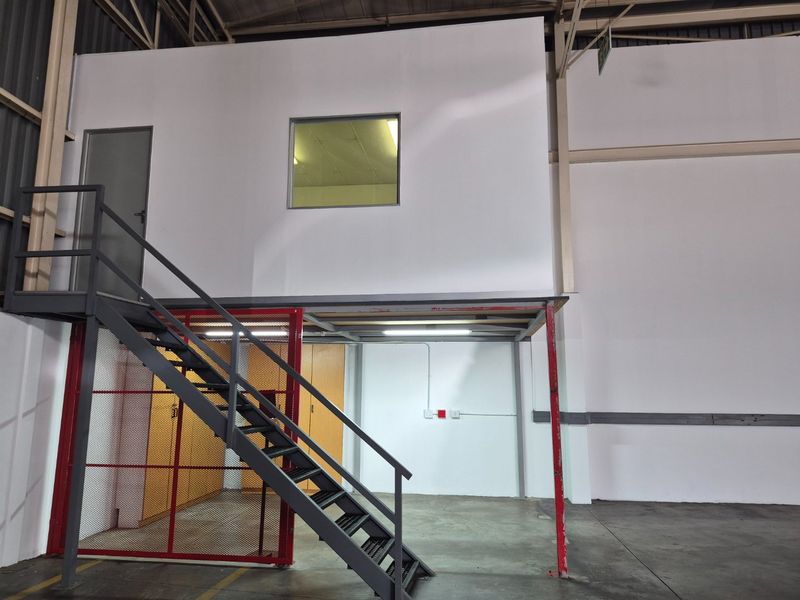 Industrial warehouse space featuring a mezzanine level with a metal staircase, secure mesh enclosure, and integrated office area with internal window.