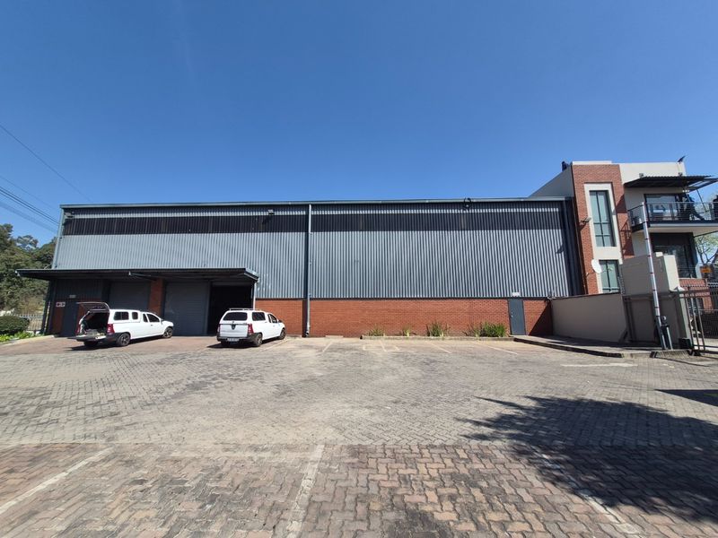 Industrial warehouse facility featuring a large corrugated metal and brick facade with multiple roller shutter doors and an expansive paved parking area.