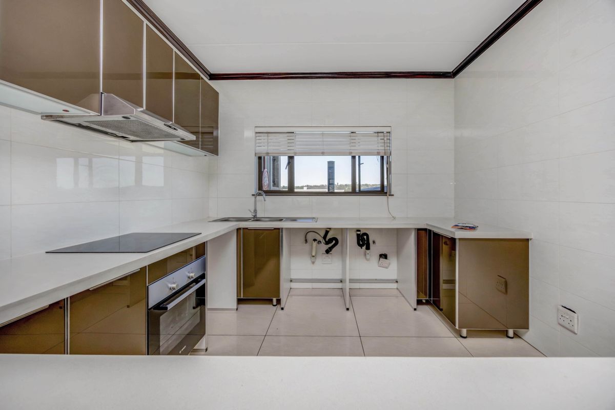 A functional kitchen featuring built-in cabinetry, an electric hob, oven, extractor fan, and tiled finishes, ready for final appliance installation.