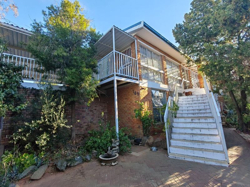 Front elevation of a multi-level brick house featuring an elevated balcony, external staircase, and paved driveway area.