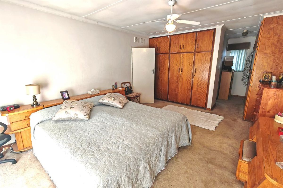 Spacious bedroom featuring extensive built-in wooden cabinetry, a ceiling fan, and carpeted flooring, offering a functional layout with potential for modernization.
