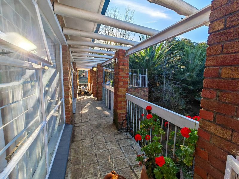 A covered outdoor patio featuring exposed brick pillars, a timber pergola, and tiled flooring, offering a view of the surrounding garden area.