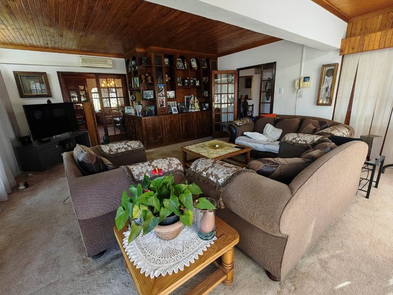 Spacious living room featuring a timber-paneled ceiling, built-in wooden cabinetry, and split-system air conditioning, offering a traditional and cozy atmosphere.