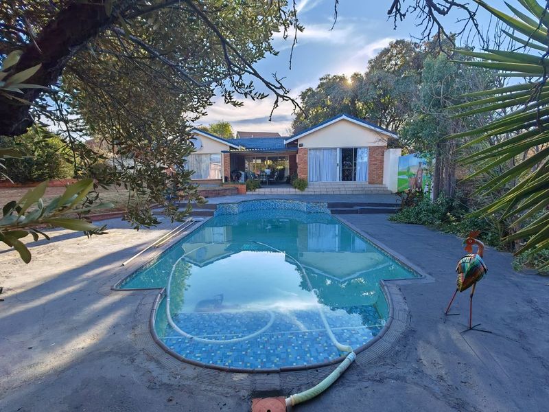 A backyard view featuring a swimming pool with tiled finish, set against a brick house with a covered patio and sliding door access.