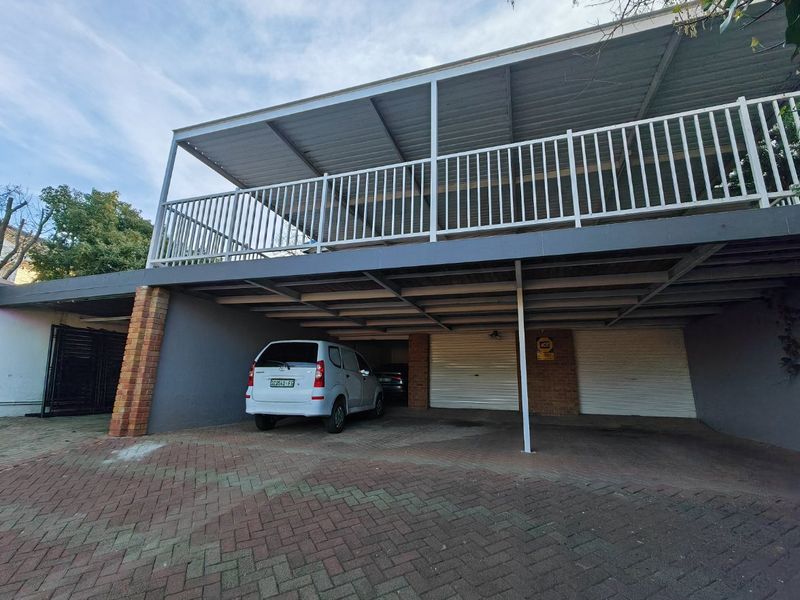 A double garage with a paved driveway and a covered balcony above, featuring metal railings and brick structural supports.