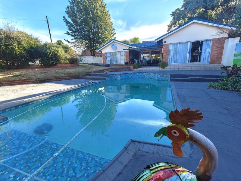 Rear view of the house featuring a swimming pool with tiled surround, concrete patio area, and brick exterior walls with sliding glass doors.