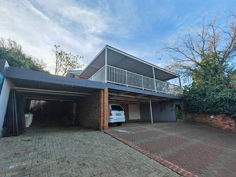 Front view of the property featuring a paved driveway, covered carport area, and an elevated balcony with metal railing.