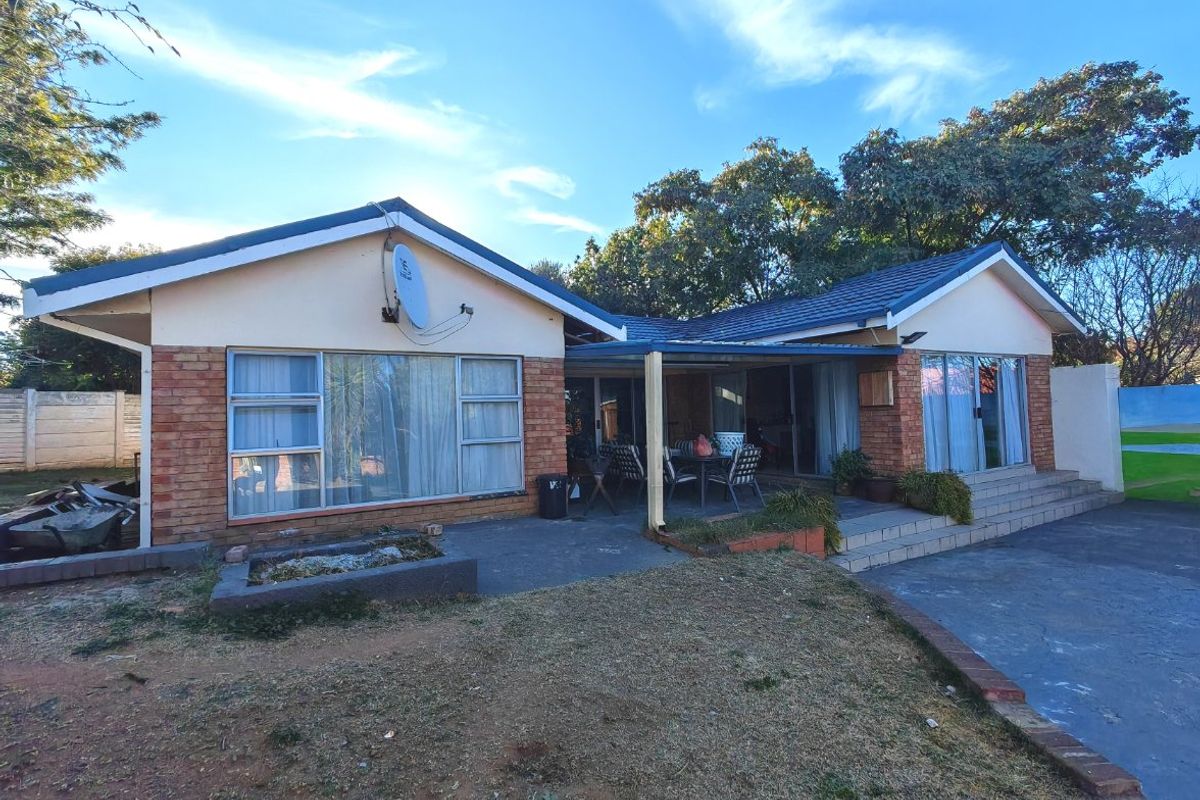 Rear view of a single-story brick house featuring a covered patio area, sliding glass doors, and a large backyard space.