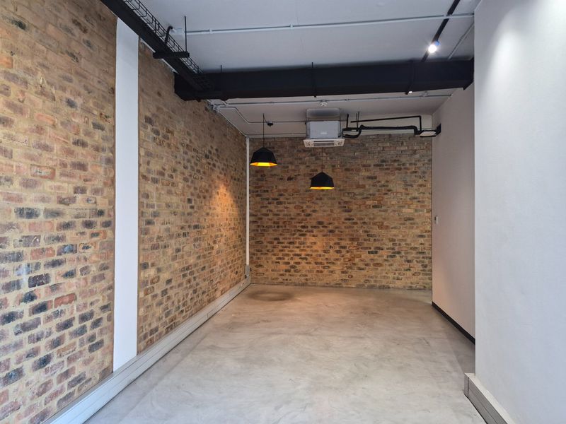 A modern, empty commercial office space featuring exposed brick walls, polished concrete flooring, and industrial-style exposed ceiling services with pendant lighting.
