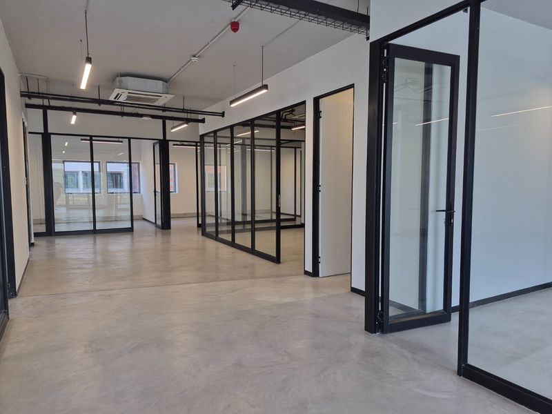 Modern open-plan commercial office space featuring polished concrete floors, black-framed glass partitioning, and exposed industrial-style ceiling services with integrated lighting.