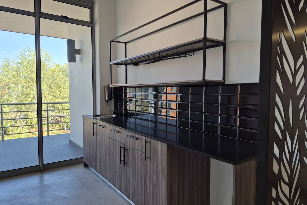 Modern kitchenette featuring wood-grain cabinetry, black stone countertops, subway tile backsplash, and industrial-style metal shelving, adjacent to a balcony access point.