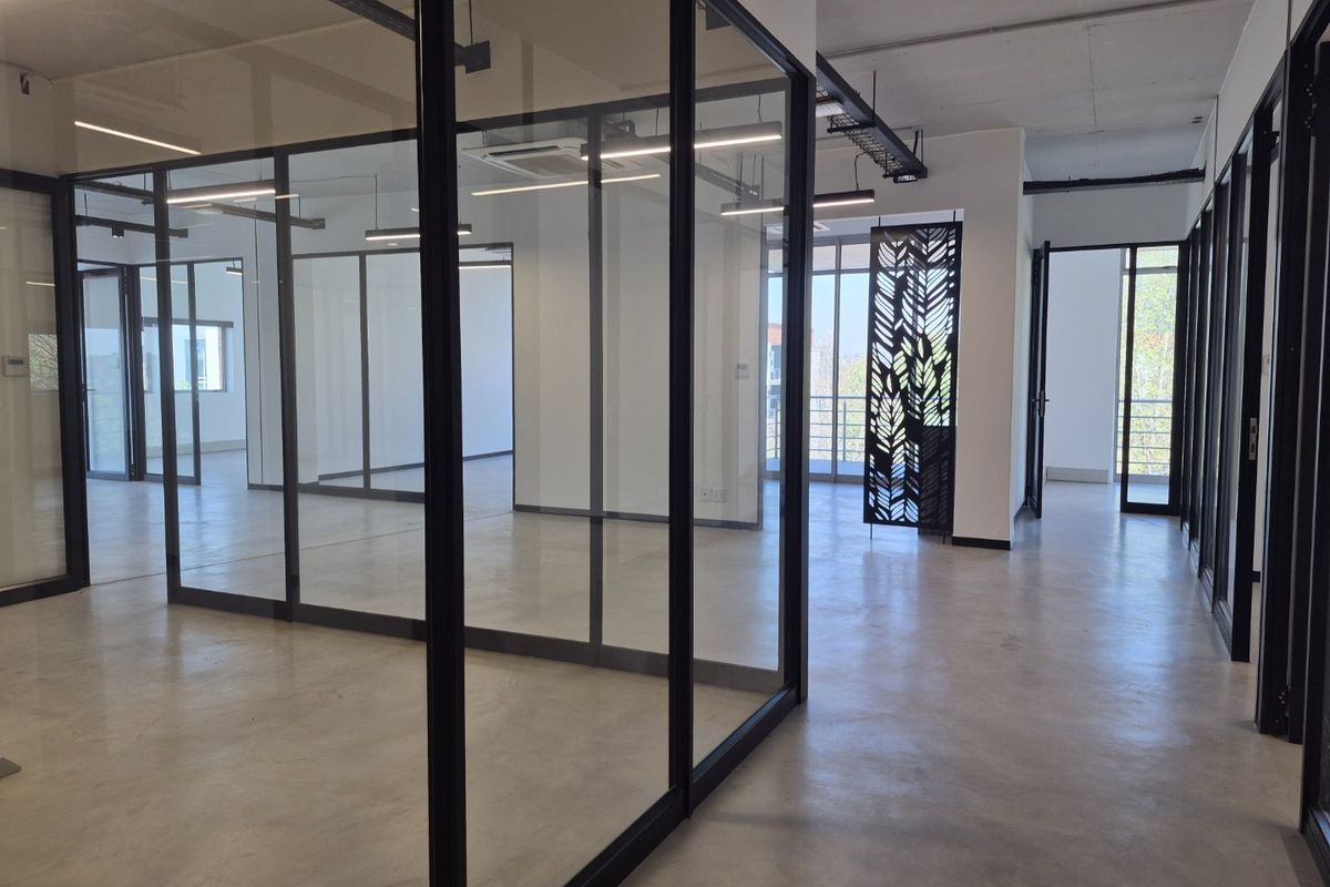 Modern open-plan office space featuring polished concrete floors, glass partitioning, and contemporary exposed ceiling design with linear lighting.