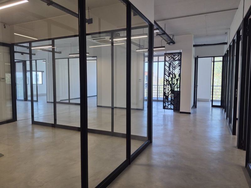 Modern open-plan office space featuring polished concrete floors, glass partitioning, and contemporary exposed ceiling design with linear lighting.