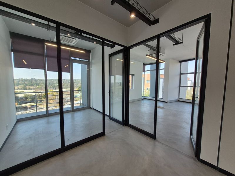 Modern open-plan office space featuring polished concrete floors, black-framed glass partitioning, and expansive windows providing natural light and scenic views.