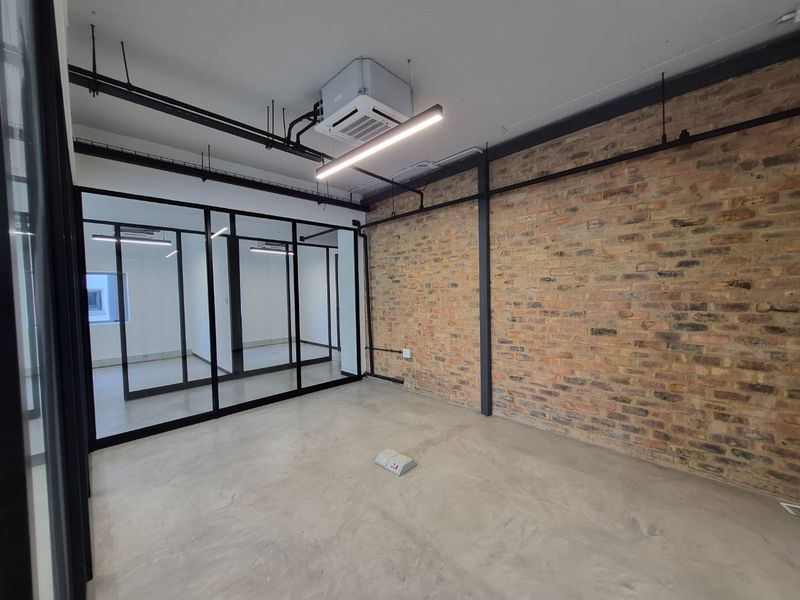 Modern industrial-style office space featuring exposed brickwork, polished concrete flooring, and sleek black-framed glass partitioning with integrated climate control.