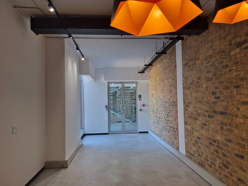Modern commercial hallway featuring polished concrete flooring, an exposed brick feature wall, and industrial-style track lighting leading to a glass entrance door.