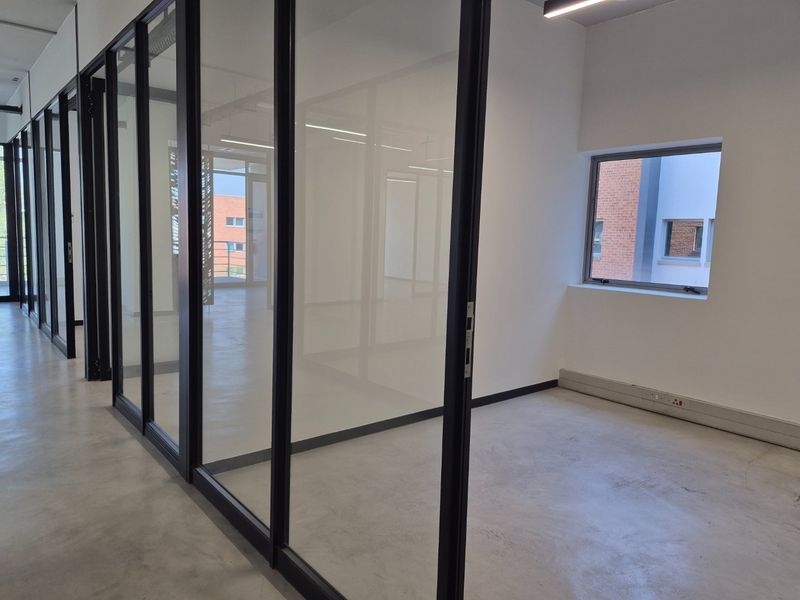 Modern commercial office space featuring polished concrete floors, black aluminum glass partitions, and clean white walls, offering a bright and professional work environment.