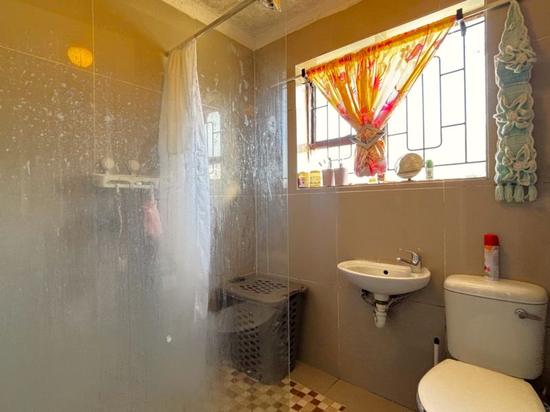 A compact bathroom featuring a shower enclosure, wall-mounted basin, and toilet with tiled wall finishes.
