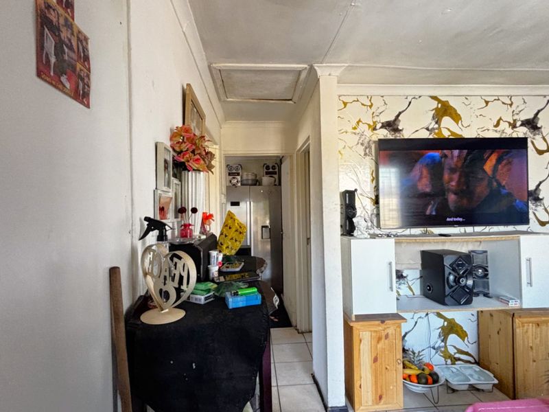 A living room area featuring tiled flooring, a decorative feature wall, and a ceiling access hatch, showing signs of wear and requiring cosmetic updates.