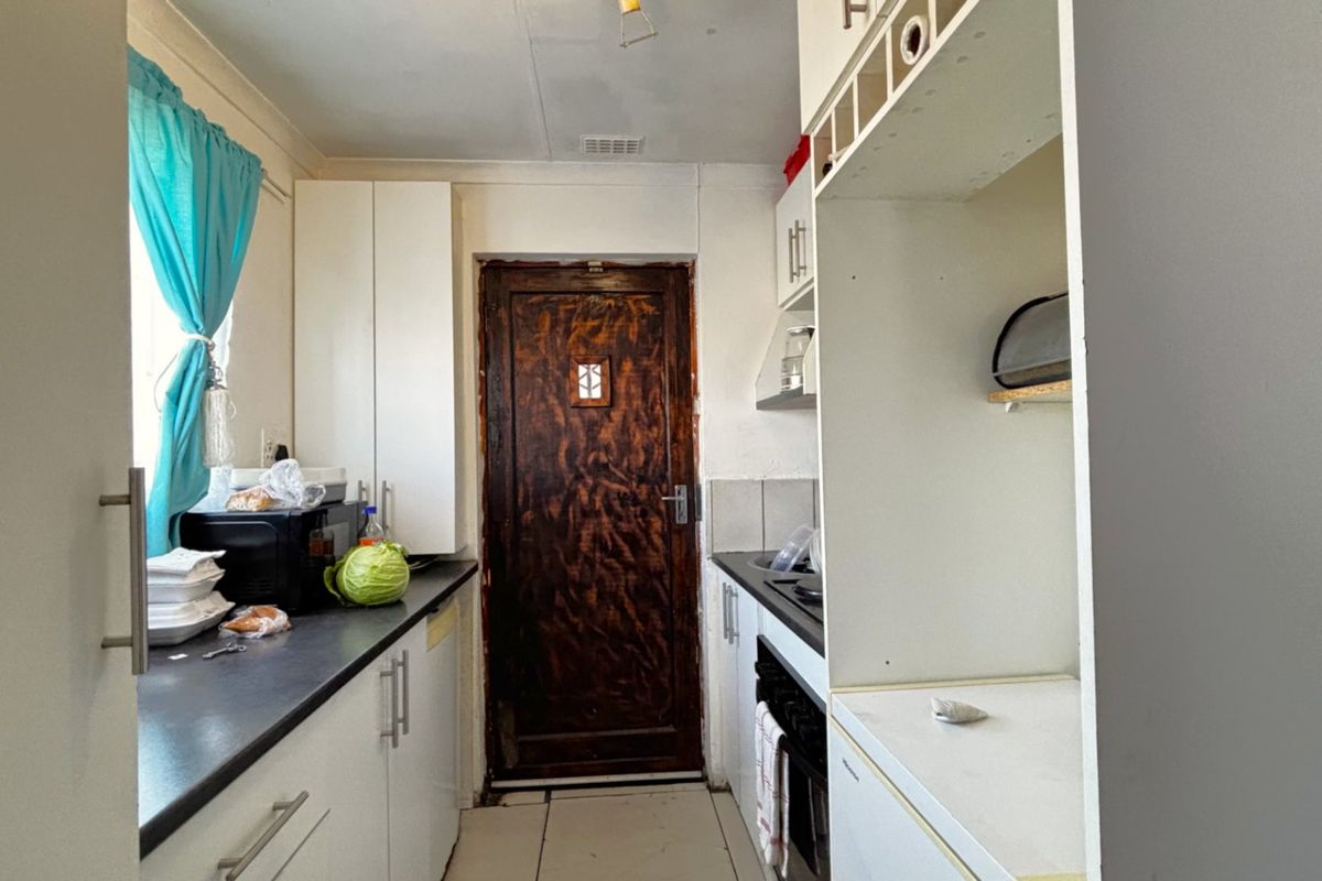 A compact kitchen featuring white built-in cabinetry, dark countertops, and a built-in oven, requiring some cosmetic updates to the door and finishes.