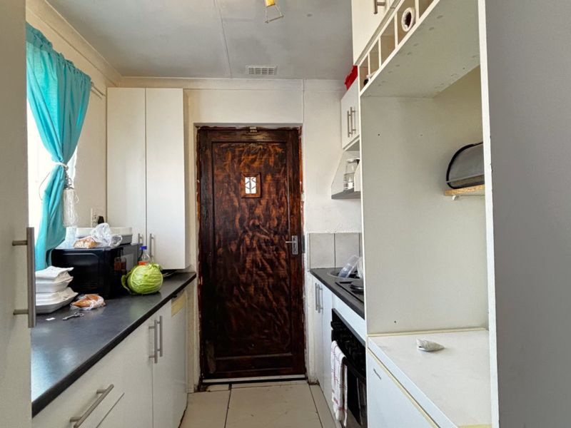 A compact kitchen featuring white built-in cabinetry, dark countertops, and a built-in oven, requiring some cosmetic updates to the door and finishes.