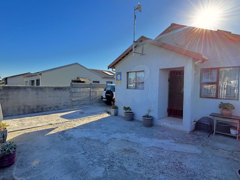 Front exterior view of the property featuring a concrete driveway, security gate, and boundary wall, with visible wear on the exterior surfaces.