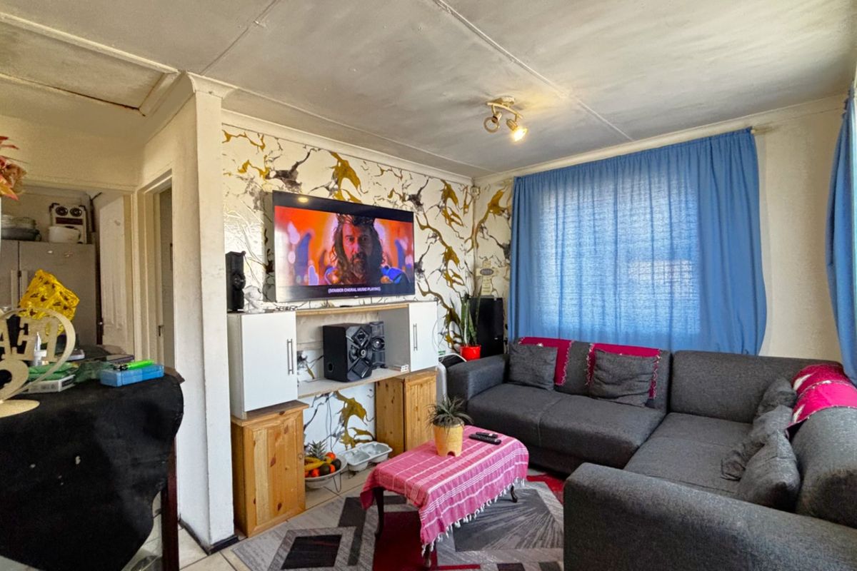 A living room featuring tiled flooring and built-in shelving, currently showing signs of wear on the ceiling and wall finishes.