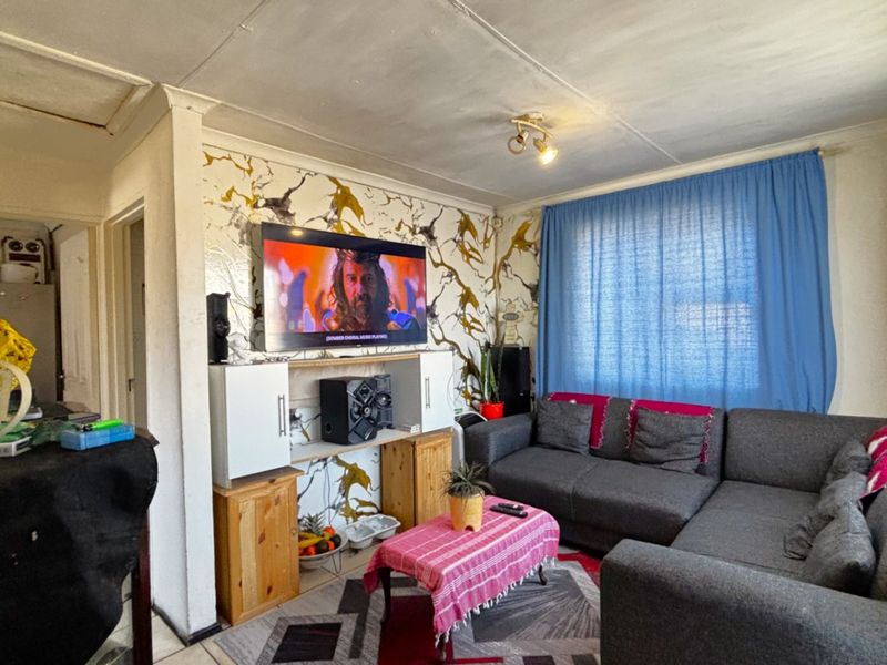A living room featuring tiled flooring and built-in shelving, currently showing signs of wear on the ceiling and wall finishes.
