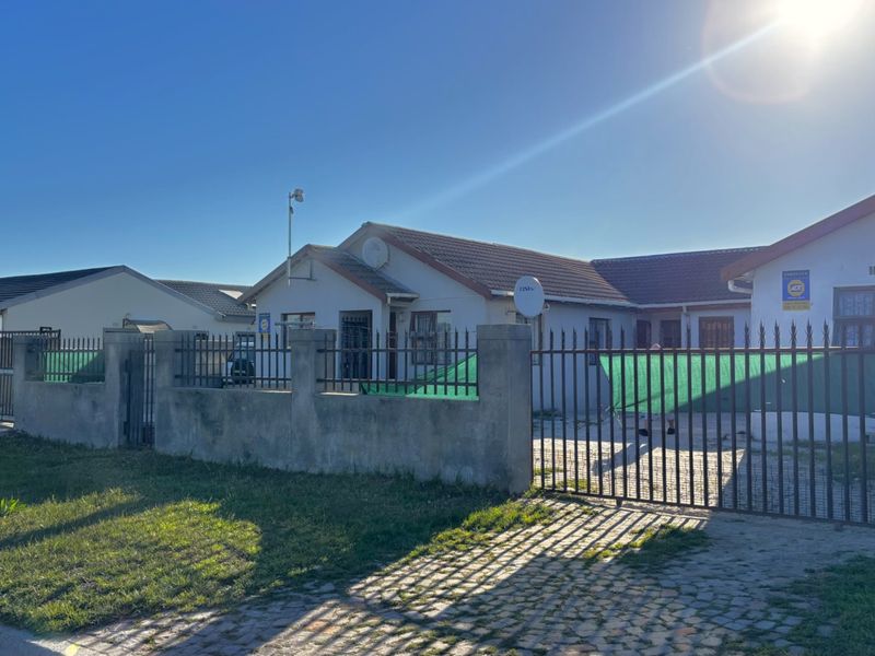Front exterior view of a single-story house featuring a concrete perimeter wall, metal security gate, and a paved driveway.