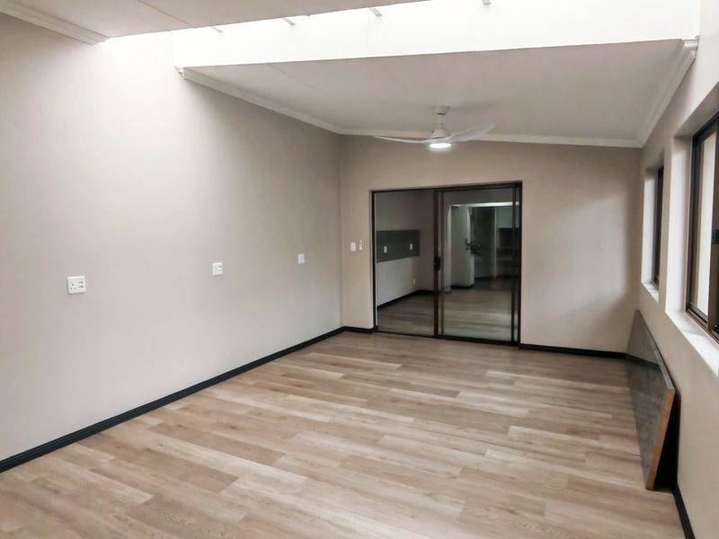 A bright, empty living area featuring modern laminate flooring, a ceiling fan, and a large skylight, providing a clean and versatile space.