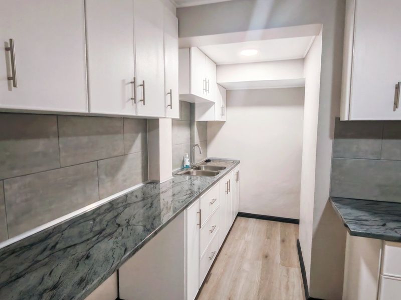 A modern, clean kitchen featuring white cabinetry, dark stone countertops, grey tiled backsplash, and light wood-look flooring.