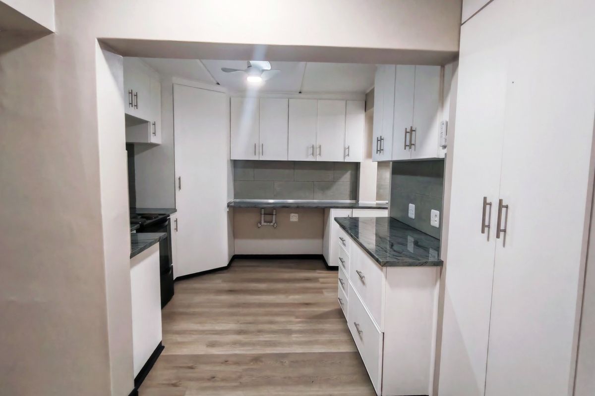 A clean, modern kitchen featuring white cabinetry, dark laminate countertops, tiled backsplash, and wood-look laminate flooring.