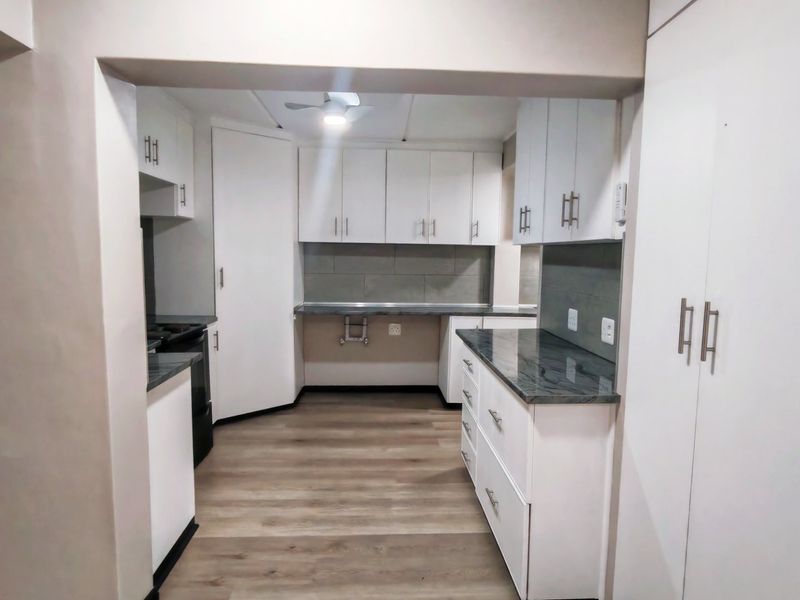 A clean, modern kitchen featuring white cabinetry, dark laminate countertops, tiled backsplash, and wood-look laminate flooring.