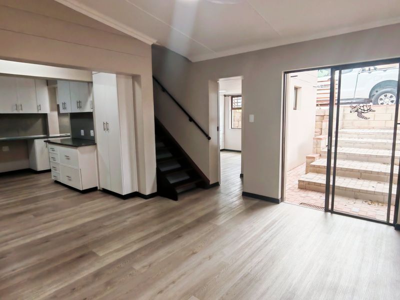 An open-plan living area featuring modern laminate flooring, a functional kitchen with built-in cabinetry, a staircase, and sliding door access to an outdoor patio.