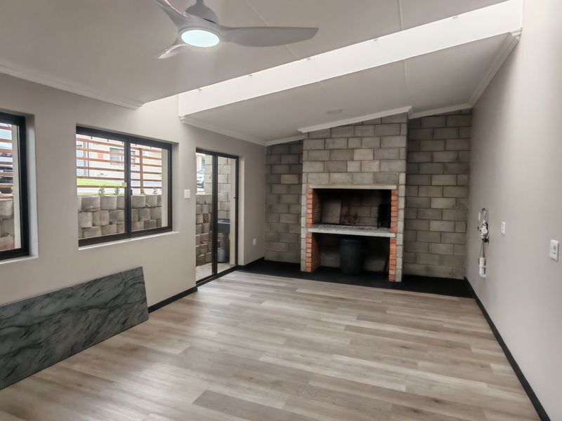 A spacious, modern enclosed patio featuring a built-in brick braai, laminate flooring, a ceiling fan, and a large skylight for natural light.